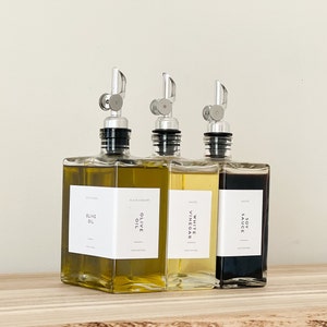 May include: Three glass bottles with pour spouts and labels. The bottles contain olive oil, white vinegar, and soy sauce.