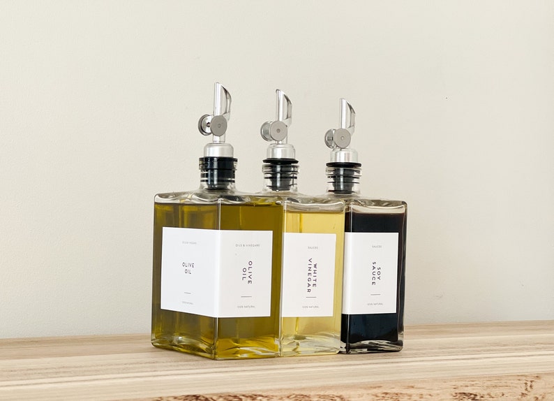 May include: Three glass bottles with pour spouts and labels. The bottles contain olive oil, white vinegar, and soy sauce.