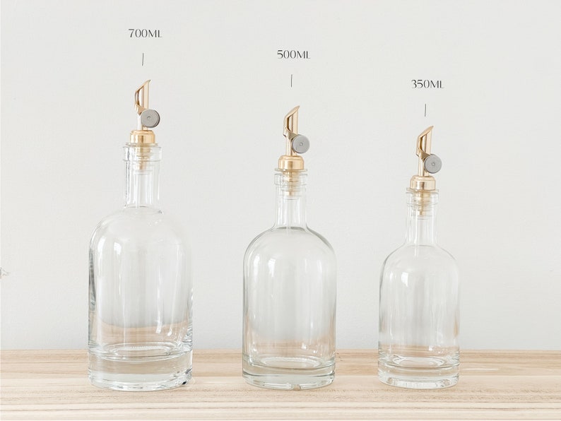 K&ouml;nnte beinhalten: Drei Glasflaschen mit goldenen Ausg&uuml;ssen und klaren Glask&ouml;rpern. Die Flaschen sind mit 700 ml, 500 ml und 350 ml beschriftet.