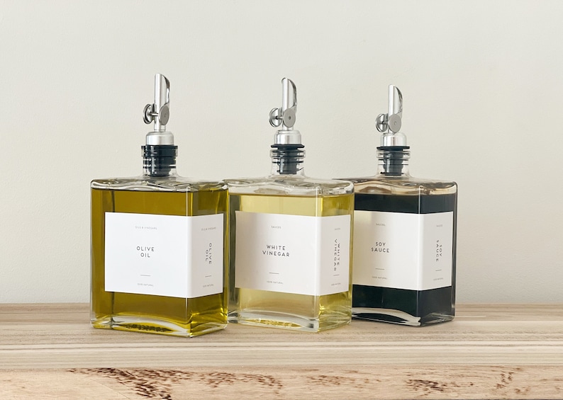 May include: Three glass bottles with silver pour spouts and labels. The bottles contain olive oil, white vinegar, and soy sauce.