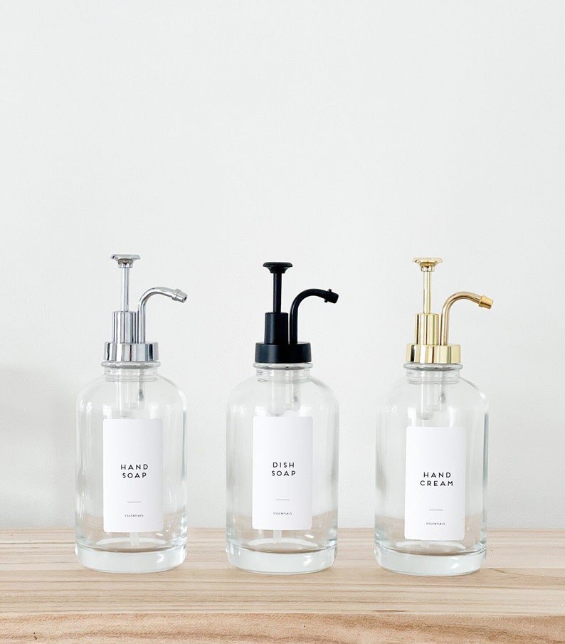 May include: Three glass bottles with pumps and labels. The bottles are filled with liquid. The labels read "Hand Soap", "Dish Soap", and "Hand Cream".
