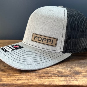 May include: A gray and black trucker hat with a brown leather patch that says "POPPI" on it.