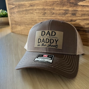 May include: A brown and beige trucker hat with a brown patch that reads "Dad in the streets, Daddy in the sheets".