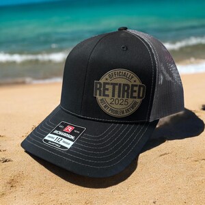 May include: Black and gray trucker hat with a gold patch that says "Officially Retired 2025 Not My Problem Anymore".
