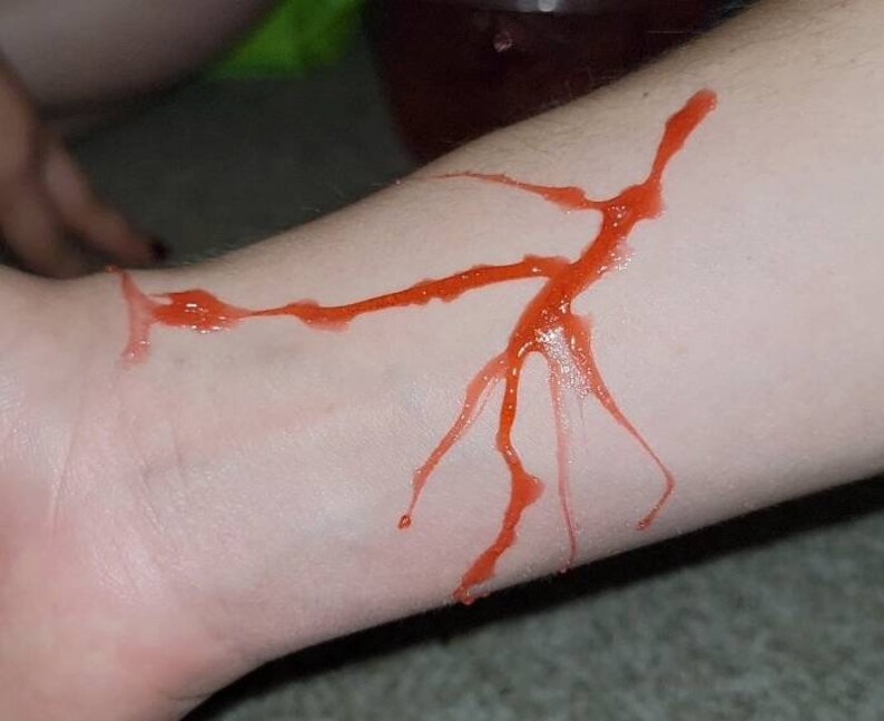 May include: A close-up of a person's arm with a red, fake blood-like substance smeared on it. The substance is in the shape of a jagged line and branches.