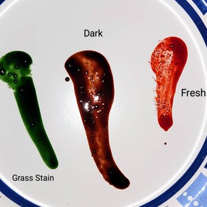 May include: Three drops of liquid on a white plate. The drop on the left is green and labeled "Grass Stain". The drop in the middle is dark brown and labeled "Dark". The drop on the right is red and labeled "Fresh".