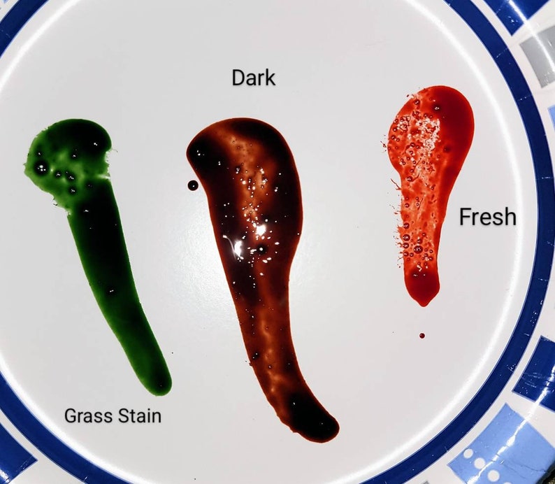 May include: Three drops of liquid on a white plate. The drop on the left is green and labeled "Grass Stain". The drop in the middle is dark brown and labeled "Dark". The drop on the right is red and labeled "Fresh".