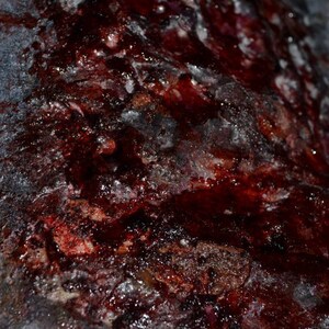 May include: Close-up of a textured surface with a dark red, almost black, color. The surface is covered in a thick layer of a white substance, possibly dried blood or paint. The texture is rough and uneven, with a variety of bumps and ridges.