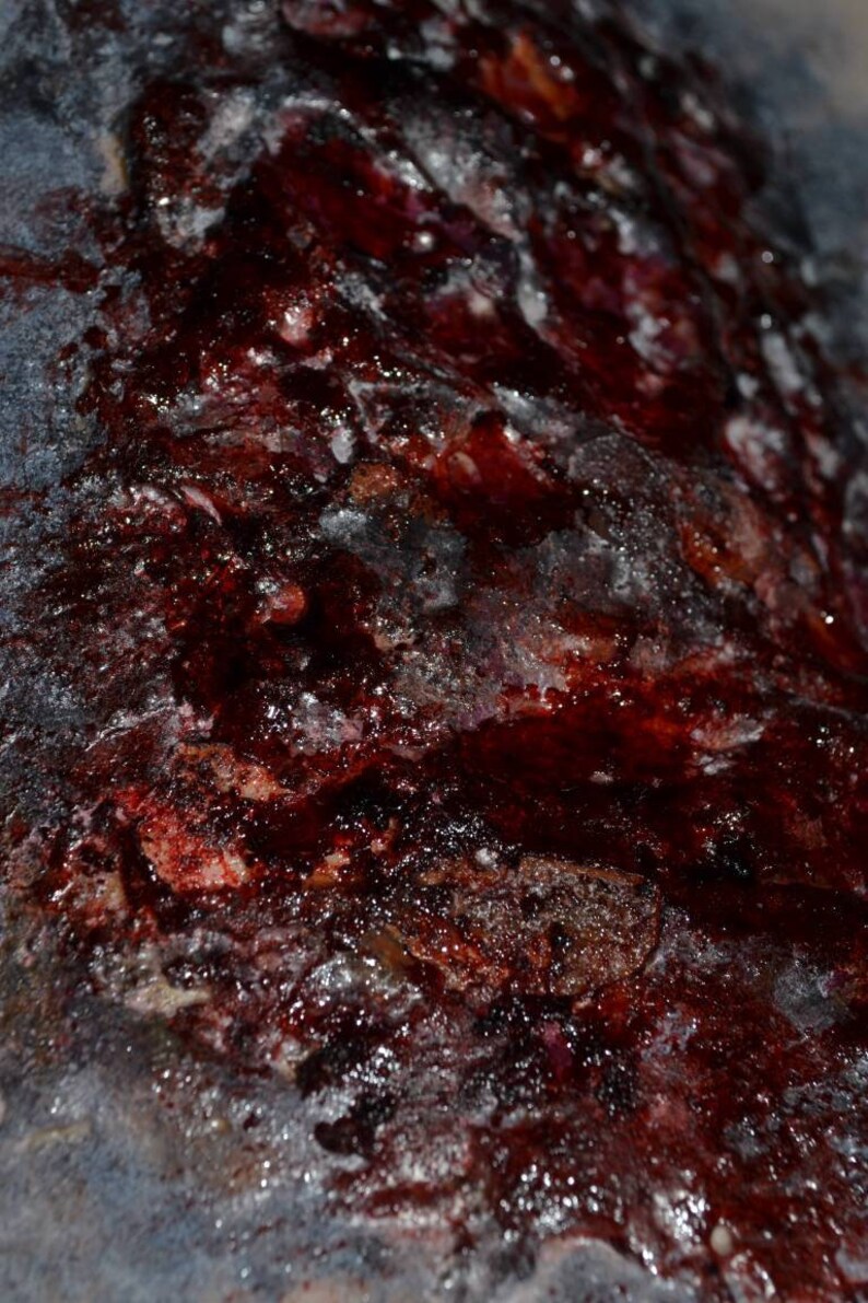 May include: Close-up of a textured surface with a dark red, almost black, color. The surface is covered in a thick layer of a white substance, possibly dried blood or paint. The texture is rough and uneven, with a variety of bumps and ridges.