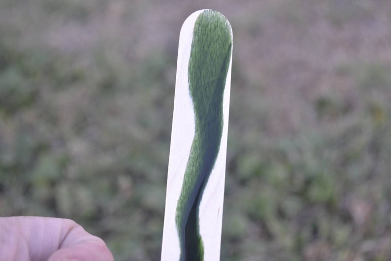 May include: A white stick with a green liquid inside. The liquid is a dark green color and has a wavy pattern.