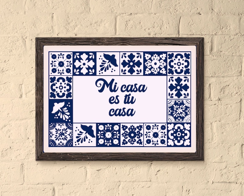 May include: A framed print with a white background and blue and white tile patterns around the edges. The text "Mi casa es tu casa" is written in a blue cursive font in the centre of the print.