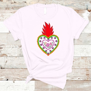 May include: White t-shirt with a red, orange, green, purple, and pink embroidered heart with flowers. The heart is a traditional Mexican folk art design.