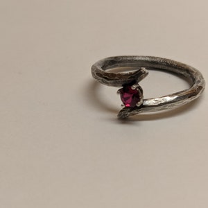 May include: A silver ring with a textured band and a single red gemstone set in the center.