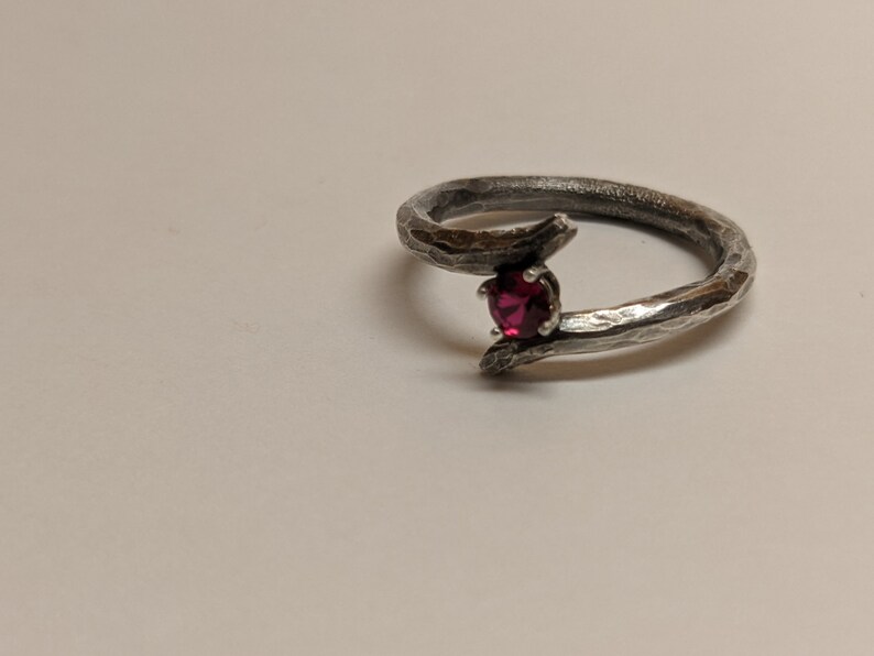 May include: A silver ring with a textured band and a single red gemstone set in the center.