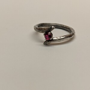 May include: A silver ring with a textured band and a single red gemstone.