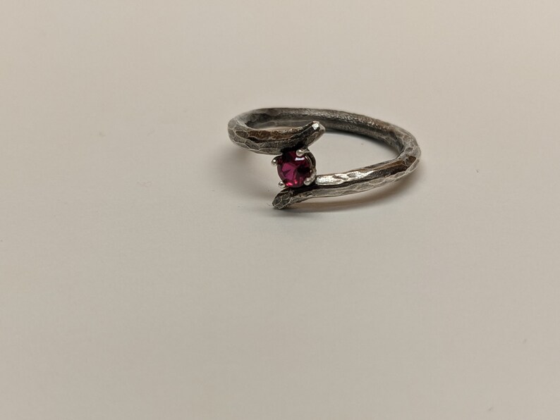 May include: A silver ring with a textured band and a single red gemstone.