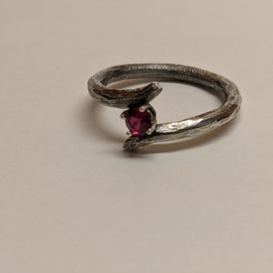 May include: A silver ring with a textured, branch-like design and a single red gemstone.