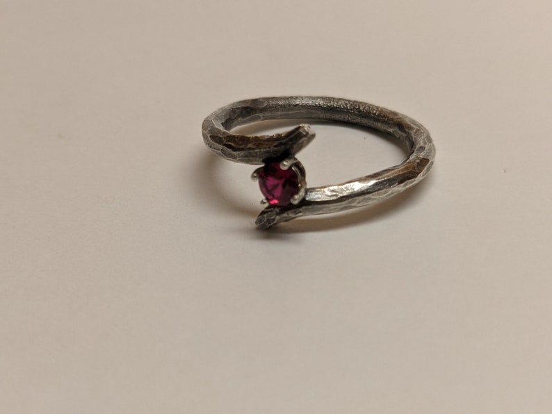 May include: A silver ring with a textured, branch-like design and a single red gemstone.