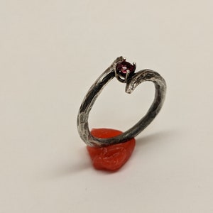 May include: A silver ring with a textured, branch-like design and a single red gemstone set in the center.
