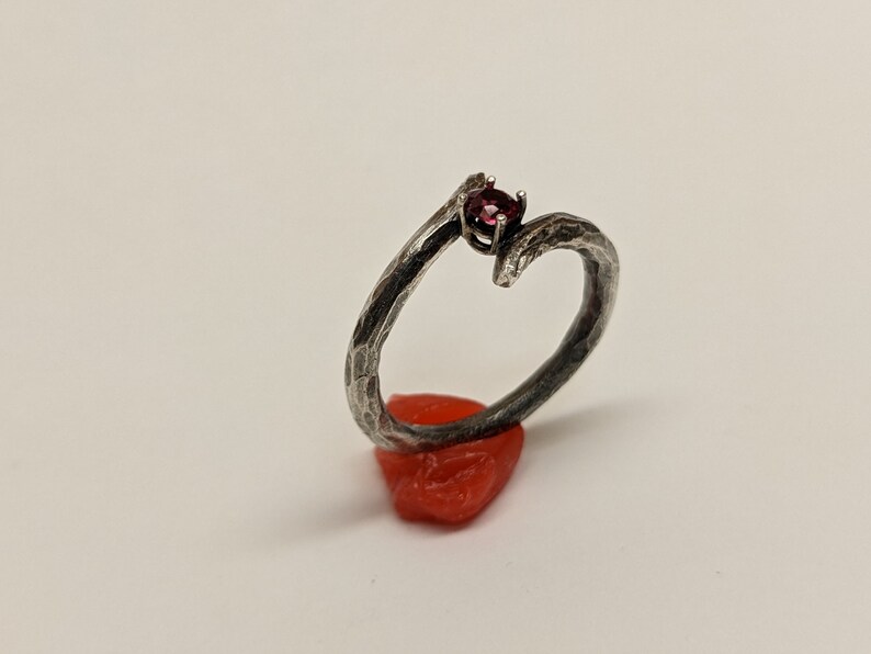 May include: A silver ring with a textured, branch-like design and a single red gemstone set in the center.