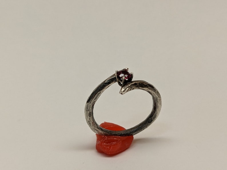 May include: A silver ring with a textured finish and a single red gemstone set in the center.