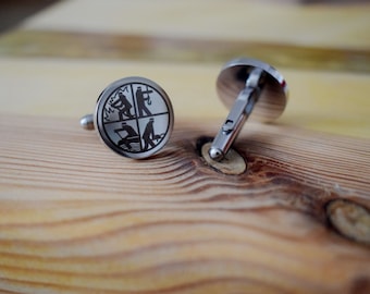 May include: A pair of silver cufflinks with a circular design featuring four black silhouettes of people engaged in different activities. The cufflinks are on a wooden surface.