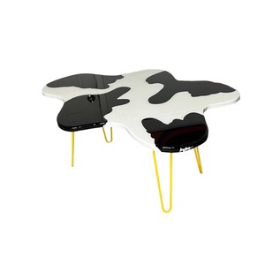 May include: A black and white cow print coffee table with a unique, irregular shape and gold hairpin legs.