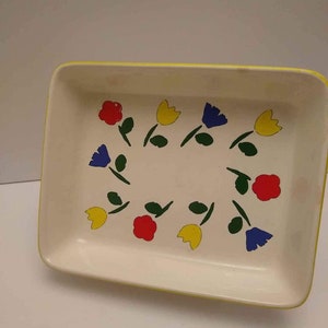 May include: A white ceramic baking dish with a yellow rim and a floral design. The flowers are red, yellow, blue, and green.