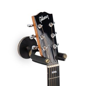 May include: Black guitar wall mount with a Gibson guitar hanging on it. The guitar has a black body and a brown fretboard.