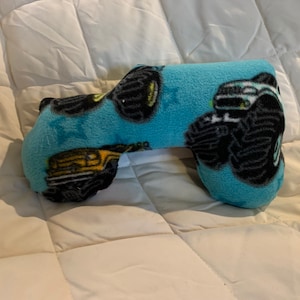 May include: A blue and black monster truck themed neck pillow. The pillow is shaped like a neck pillow and has a monster truck design on it.