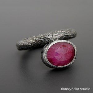 Può includere: Un anello d'argento con una fascia testurizzata e una grande pietra preziosa di rubino di forma ovale.