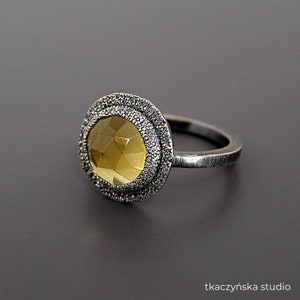 May include: A silver ring with a yellow gemstone set in a textured silver bezel. The ring has a simple band.