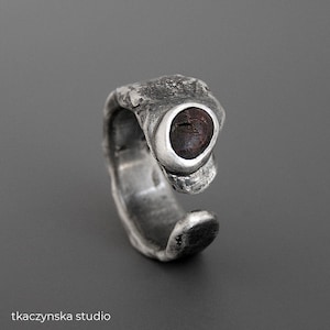 Op de afbeelding: Een zilveren ring met een getextureerd, organisch ontwerp. De ring heeft een donkerbruine steen die is gezet in een zilveren bezel.