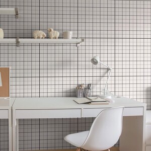 May include: A white desk with a white chair in front of it. The desk has a white lamp on the right side and a white shelf above it. The wall behind the desk is covered in a white and black grid pattern wallpaper.