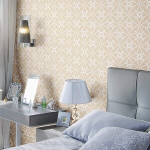 May include: A bedroom with a beige patterned wallpaper, a gray headboard, and a white lamp on a nightstand. The bed has a gray and white patterned pillow and a white pillow.
