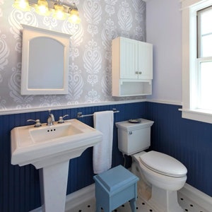 May include: A white bathroom with blue wainscoting and a white vanity with a pedestal sink. The bathroom has a white toilet, a white medicine cabinet, and a blue stool.