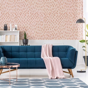 May include: A teal blue sofa with a pink throw blanket in a living room with a pink and brown patterned wallpaper. The sofa is in front of a white bookshelf with books and a potted plant.