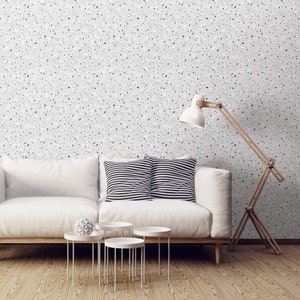 May include: A white couch with two black and white striped pillows sits in front of a white wall with a black and white speckled pattern. A wooden floor lamp with a white shade is in the corner of the room. There are three white round side tables in front of the couch.