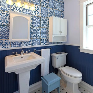 May include: A small bathroom with blue and white patterned tile walls, a white pedestal sink, a white toilet, and a white cabinet with a shelf. The floor is black and white checkered tile.