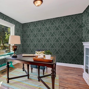 May include: A home office with a dark green damask wallpaper, a wooden desk with a chair, a lamp, and a potted plant.