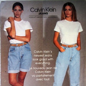 May include: A vintage Vogue Patterns sewing pattern featuring two models wearing denim jeans. The pattern is for Calvin Klein jeans and the text on the pattern reads "Calvin Klein Jeans, Vogue American Designer".