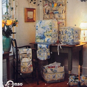 May include: A Simplicity Crafts sewing pattern envelope 8826 featuring various fabric storage organisers with a blue and yellow floral and plaid pattern, including a wall hanging, appliance covers, a chair pocket, and a basket liner.