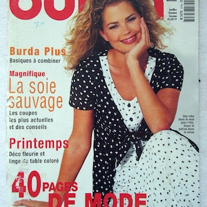 Op de afbeelding: Een vintage Burda magazine cover met een lachende vrouw met blond haar. De cover heeft de titel "Burda" in het rood, met Franse tekst. De vrouw draagt een zwart-witte polkadotjurk.