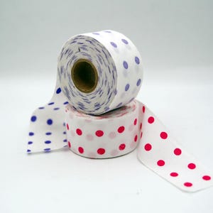 Peut inclure: Deux rouleaux de ruban en tissu blanc empilés avec des motifs à pois. Le rouleau supérieur présente des pois bleus, tandis que le rouleau inférieur présente des pois rose vif. Les deux rouleaux ont un noyau central en carton.