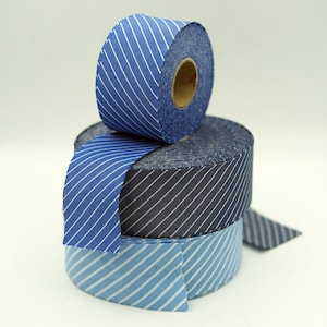 May include: Three rolls of striped ribbon in shades of blue. The rolls are stacked, with the top roll angled to show the white stripes. The ribbon is made of fabric and has a paper core.