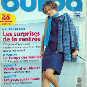 May include: A magazine cover featuring a woman wearing a blue and white plaid jacket over a dark blue dress and a light blue scarf. The magazine is titled "Burda" and the cover text reads "Les surprises de la rentrée" and "Tous à l'école!"