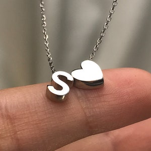 May include: Silver necklace with a heart charm and a letter 'S' charm.