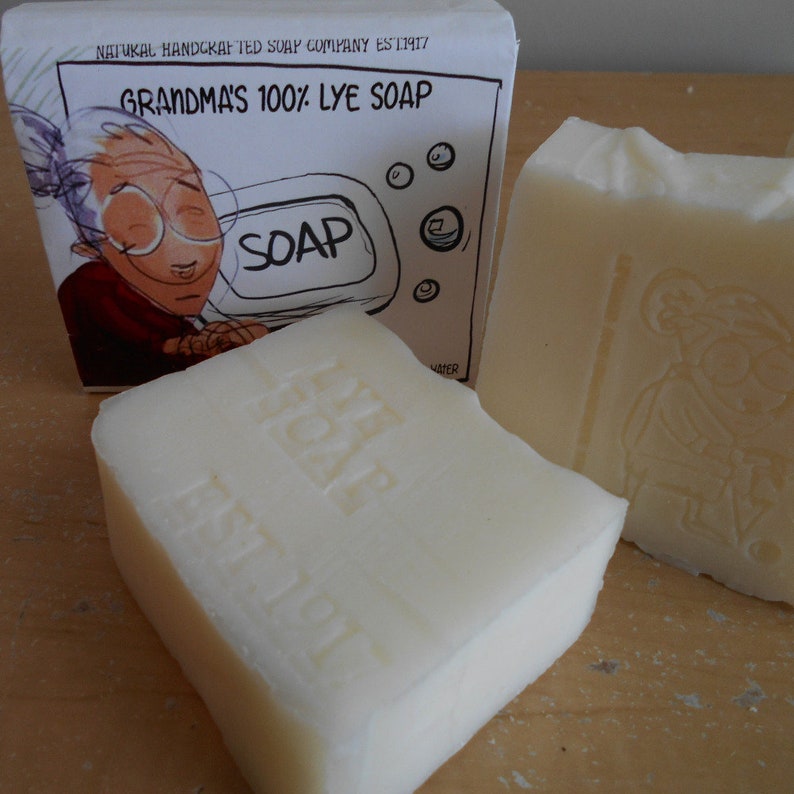 One bar is propped up and detailed with an engraved label "lye soap". The soap bars have a natural, rustic appearance with a Grandmas logo are displayed on a wooden stand.