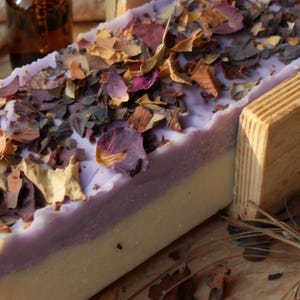 Puede incluir: Un bloque rectangular de jab&oacute;n de dos tonos con una capa base de color blanco crema y una capa superior de color violeta claro. La superficie est&aacute; cubierta con una densa dispersi&oacute;n de p&eacute;talos de flores secas en tonos rosa, rojo y marr&oacute;n.