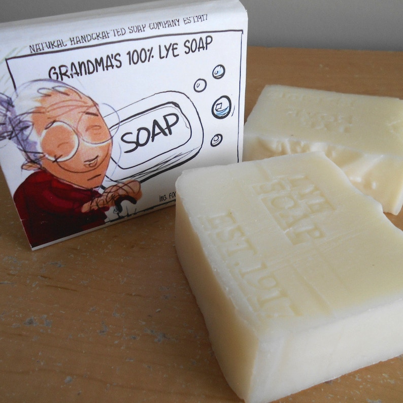 Pu&ograve; includere: Una saponetta bianca con le parole "Grandma's Soap" ed "Est. 1917" in rilievo. La saponetta &egrave; appoggiata su una superficie di legno accanto a una scatola con un'illustrazione a fumetti di una donna che tiene una saponetta.